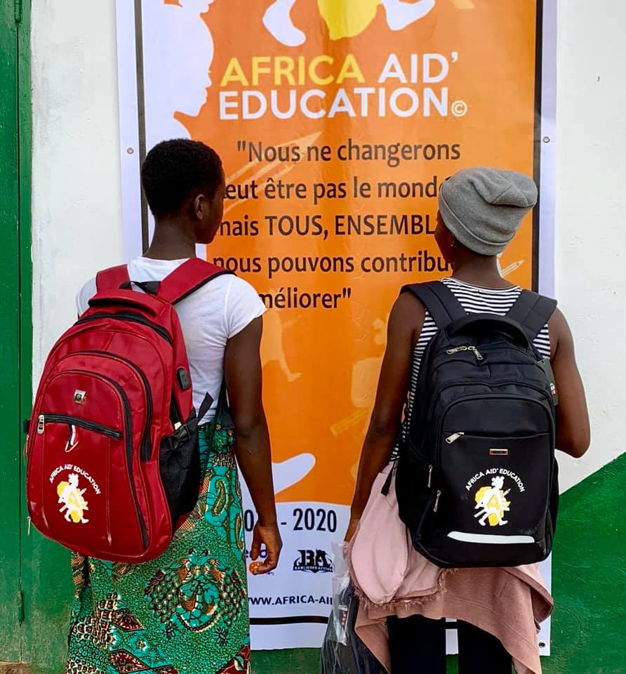 Photo de deux jeunes filles lisant l'affiche "Africa Aid' Education : "Nous ne changerons peut-être pas le monde, mais TOUS ENSEMBLE, nous pouvons contribuer à l'améliorer"